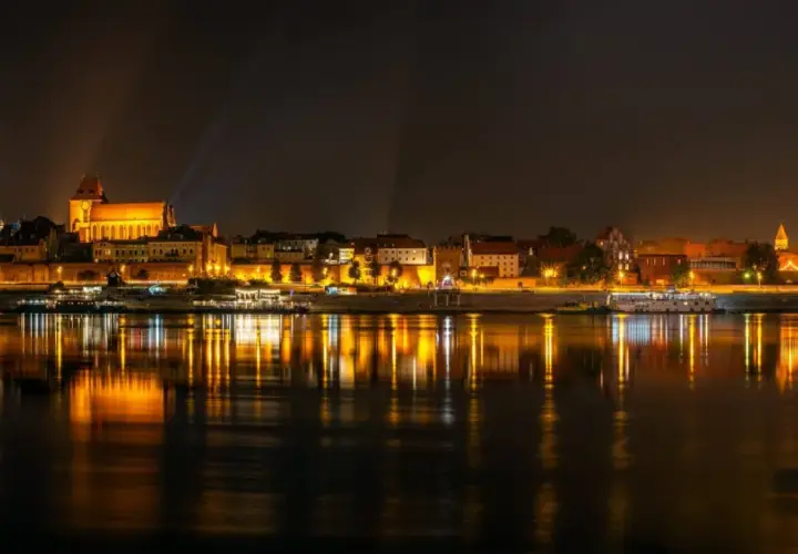 Nocny widok na oświetlony bulwar w Toruniu z odbiciem świateł w Wiśle.