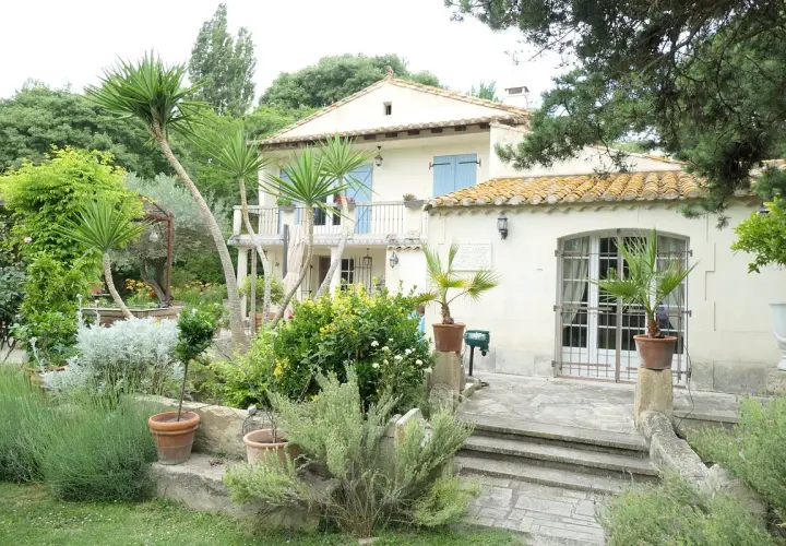 Maison en pierre avec jardin luxuriant, palmiers et lavande. Le panneau "Domaine des chênes truffiers" est visible.