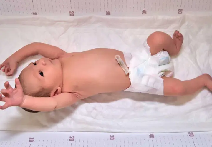 Neonato con pannolino e clip ombelicale, con le braccia sollevate, mostra i suoi riflessi neonatali su un telo con misurazioni.