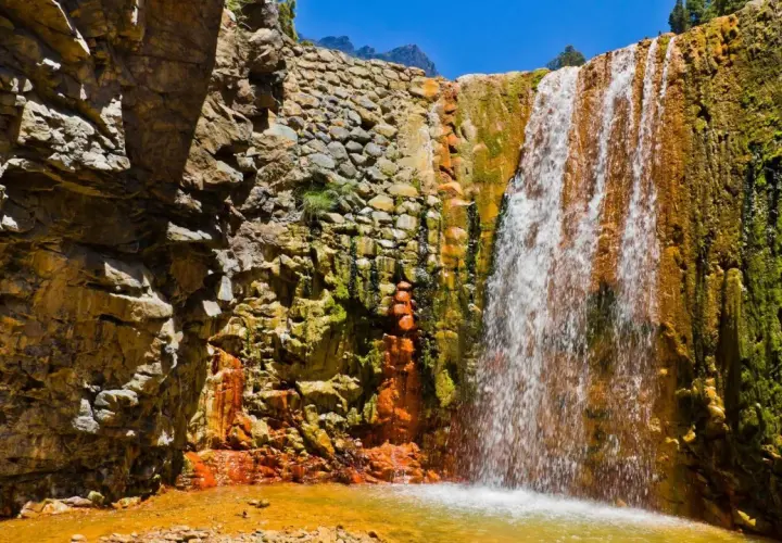 Ein Wasserfall stürzt über moosbewachsene, orangefarbene Felsen. Die Felsen sind von der Sonne beschienen, und das Wasser sammelt sich in einem goldenen Becken. Ein Stück Natur auf La Palma.