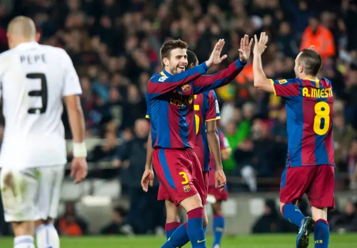 Piłkarze Barcelony, Piqué i Iniesta, świętują bramkę. Na pierwszym planie zawodnik w białej koszulce z numerem 3.