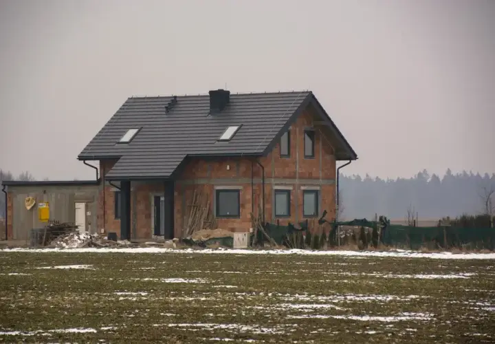 Dom w budowie, gdzie sprawdzić pozwolenie na budowę? Na placu budowy widać dom z cegły, dach i okna.