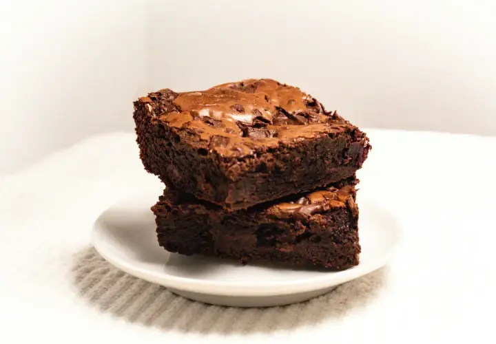 Dwa wilgotne brownie czekoladowe ułożone jedno na drugim na białym talerzyku.
