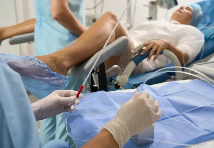 Person w rękawiczkach przygotowuje się do cewnikowania pęcherza moczowego pacjentki leżącej na fotelu ginekologicznym.