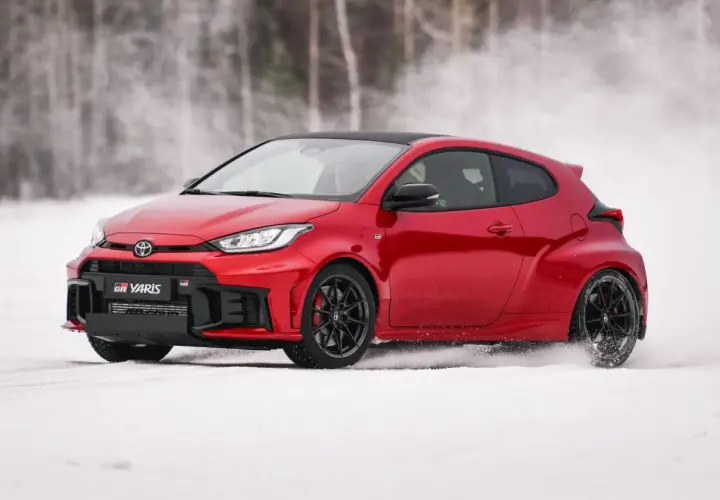 Czerwony Toyota GR Yaris driftuje po śniegu, tworząc obłoki białego puchu.