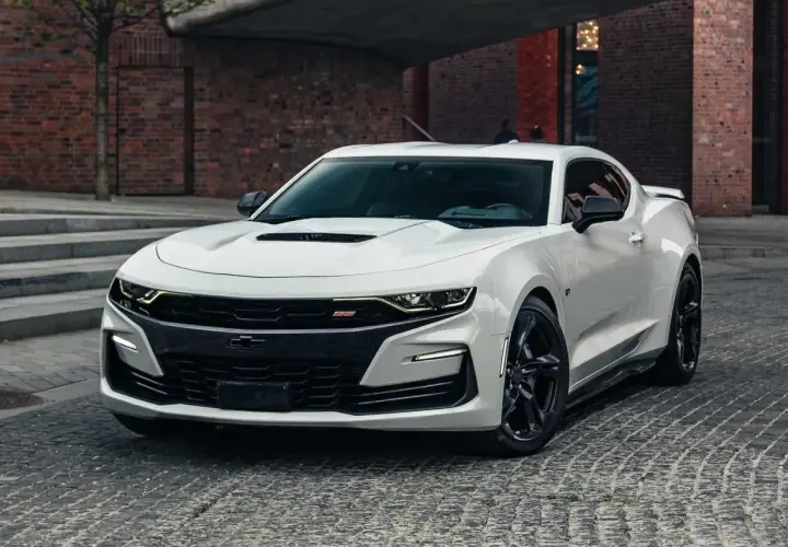 Biały Chevrolet Camaro SS z czarnymi felgami stoi na brukowanej ulicy przed ceglanym budynkiem.