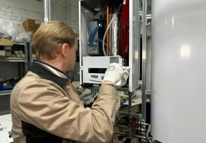 Technik w białych rękawiczkach sprawdza grzałkę miernikiem wewnątrz urządzenia.