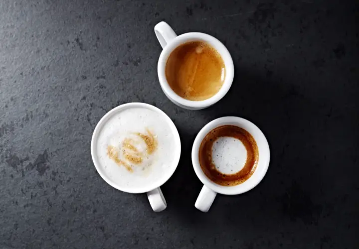 Trzy białe filiżanki z kawą: espresso, latte z wzorem i czarne espresso. Idealny poranek z parzeniem kawy.