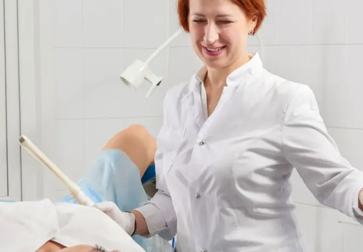 Lekarka bada pacjentkę, która leży na fotelu ginekologicznym. Specjalistka używa sondy USG, by zdiagnozować problemy, takie jak grzybica pochwy.