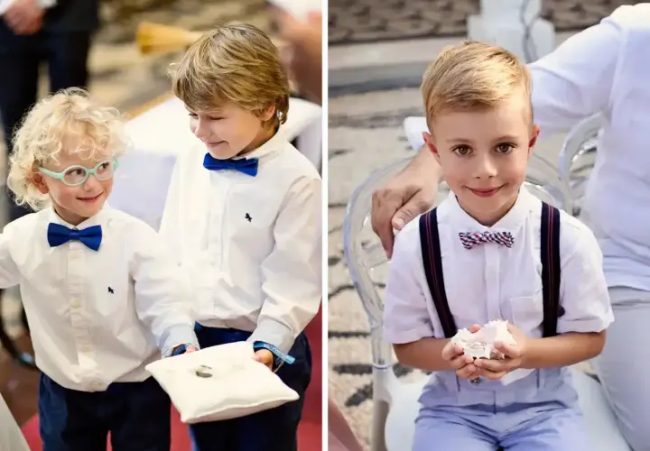 Uśmiechnięci chłopcy w eleganckich strojach, pełni powagi, niosące obrączki do ślubu. Jeden z nich ma okulary, drugi trzyma poduszkę z obrączkami.