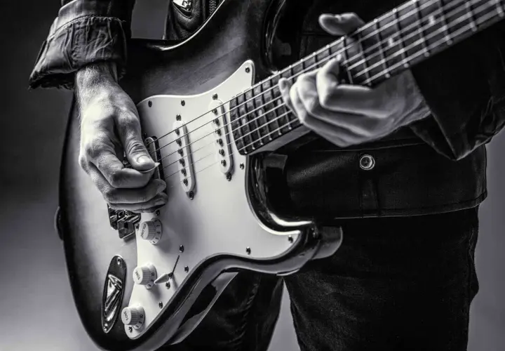 Dłoń gra na gitarze elektrycznej, ukazując klasyczne **marki gitar elektrycznych**.