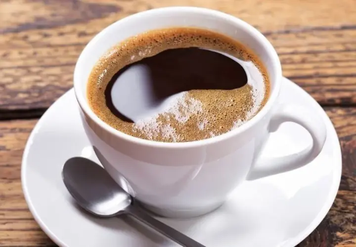 Aromatic coffee in a white cup, perfect for learning jak dobrze zaparzyć kawę sypaną. Na drewnianym blacie leży łyżeczka.