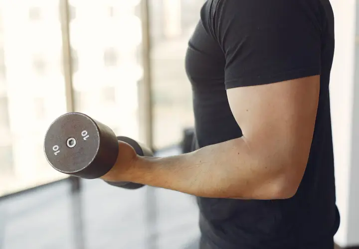 Mężczyzna wykonuje ćwiczenia na biceps i triceps z hantlem 10 kg.
