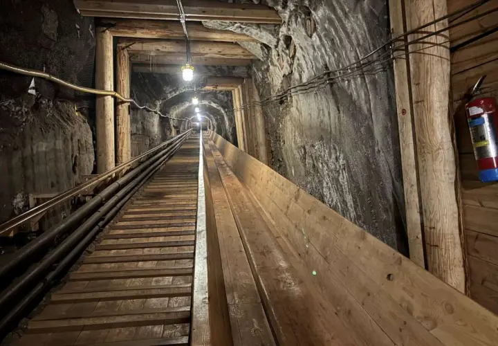 Długi, drewniany tunel w kopalni w Krakowie, oświetlony lampami, prowadzi w głąb ziemi.