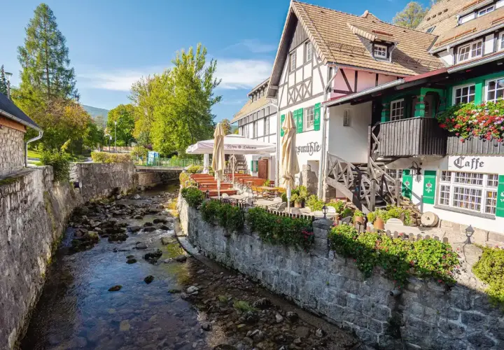 Urokliwy deptak w Szklarskiej Porębie nad kamienistym potokiem, z kawiarnią i restauracją z ogródkiem.
