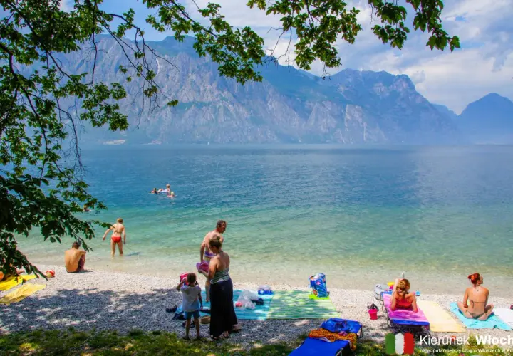 Ludzie odpoczywają na żwirowych plażach nad Jeziorem Garda, podziwiając góry.