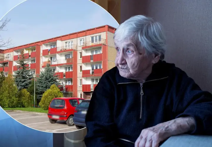 Starsza pani spogląda przez okno na blok mieszkalny, być może zastanawiając się nad swoim dodatkiem mieszkaniowym.