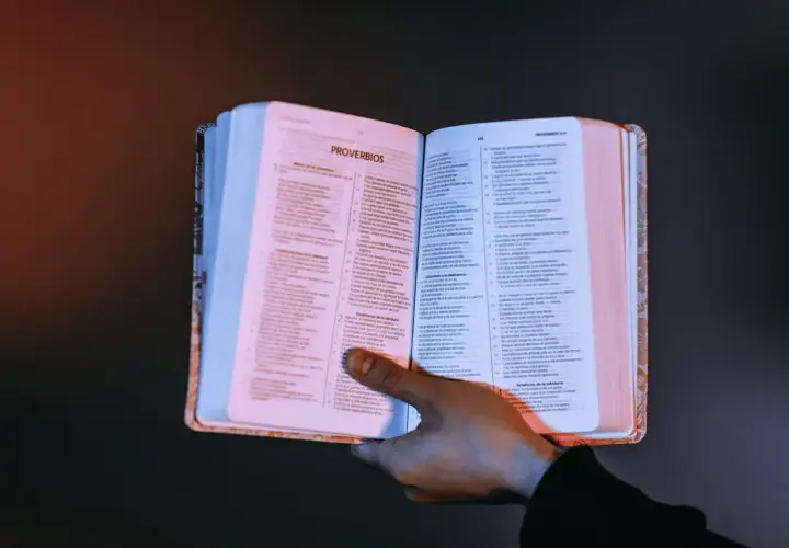 Otwarta księga z tekstem, dłoń przytrzymująca strony. Czy testament bez notariusza jest ważny? Warto szukać odpowiedzi w mądrych księgach.