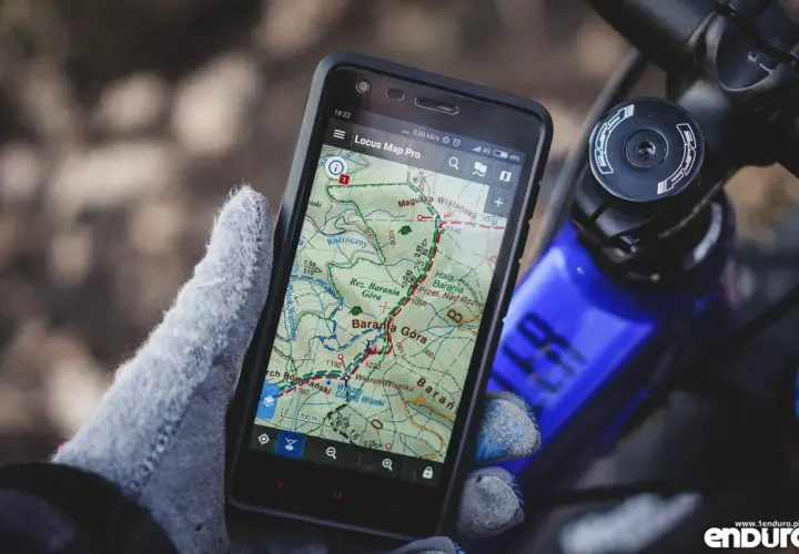 Rękawica trzyma smartfon z aplikacją szlaki turystyczne Locus Map Pro, pokazującą trasę w górach.