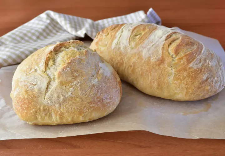 Due pagnotte di pane morbido fatto in casa, dorate e leggermente infarinate, su carta da forno.