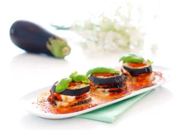 Deliciosas berenjenas a la parmesana, apiladas y cubiertas de salsa de tomate y queso fundido, adornadas con albahaca fresca.