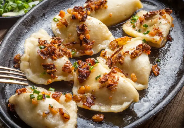 Pyszne pierogi z mięsem, okraszone skwarkami i szczypiorkiem, podane na żeliwnej patelni.