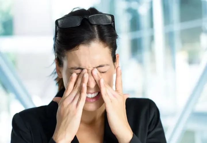 Kobieta z okularami na głowie, zaciśniętymi powiekami i dłońmi na twarzy, cierpiąca na światłowstręt.