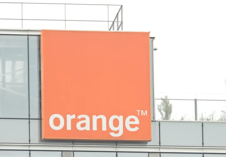 Pomarańczowy znak z napisem "orange" na nowoczesnym budynku. To logo firmy telekomunikacyjnej, która oferuje usługi multiroom.