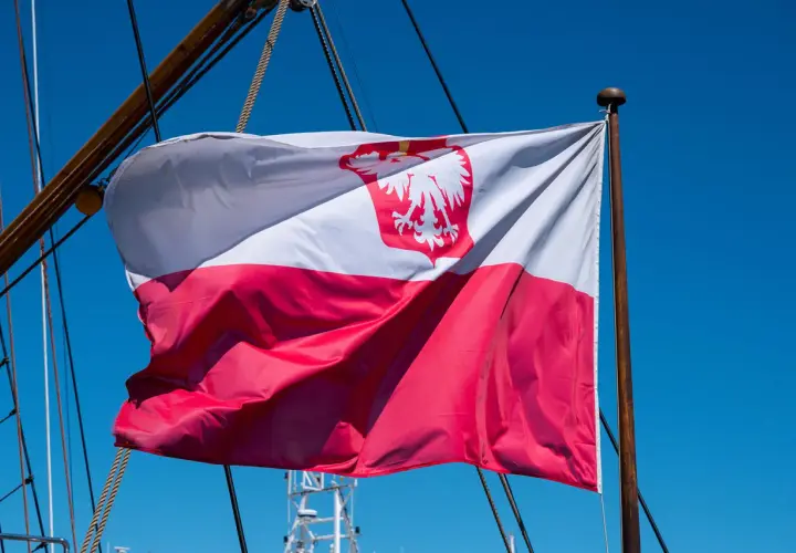Flaga bandery w Polsce, biało-czerwona z orłem, powiewa na maszcie żaglowca na tle błękitnego nieba.