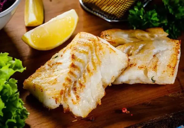 Filetti di branzino in padella in bianco, dorati e succulenti, serviti con spicchi di limone fresco e insalata croccante.