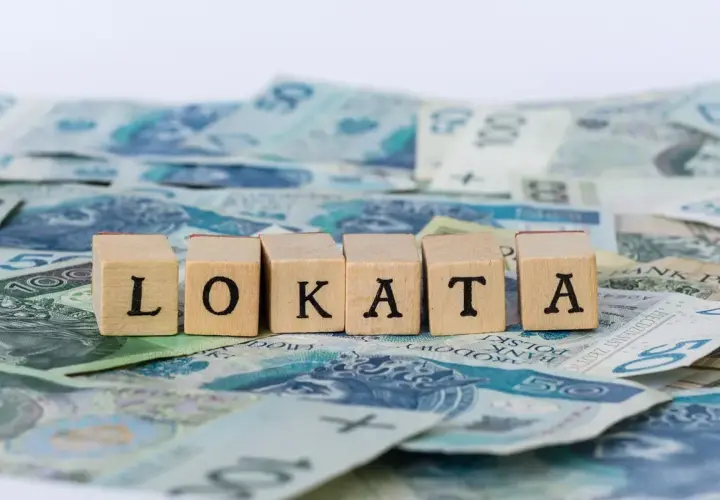Drewniane klocki z literami "LOKATA" na tle polskich banknotów.
