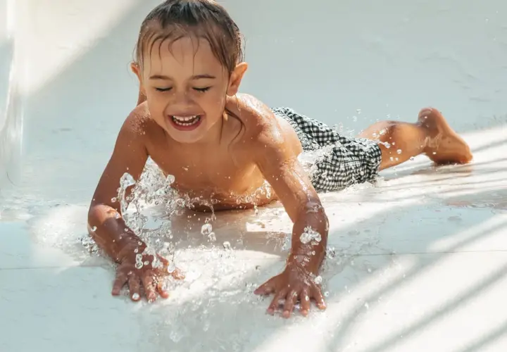 Enfant riant sur un toboggan aquatique, éclaboussures d'eau. Attention aux otites du baigneur symptômes après ces jeux !