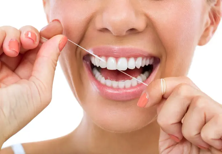 Donna sorride mentre usa il filo interdentale cerato per pulire i suoi denti bianchi e sani.