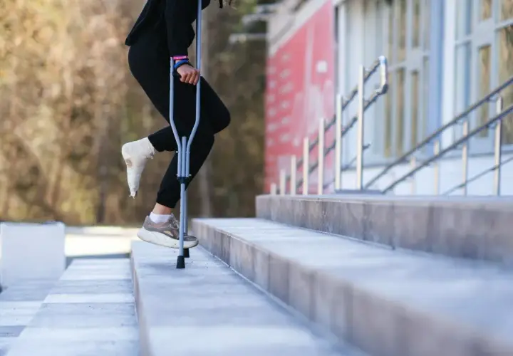 Osoba z zabandażowaną stopą porusza się po schodach, używając kul. W której ręce trzymać kulę, by było najwygodniej?