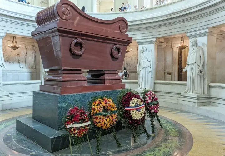 Imponujący sarkofag Napoleona, otoczony rzeźbami i wieńcami, w monumentalnym wnętrzu.