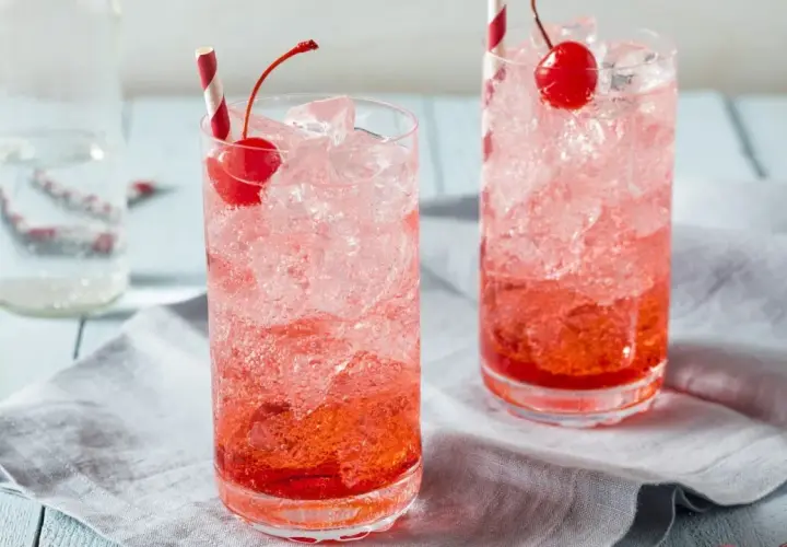Erfrischende Crodino Rezepte: Zwei Gläser mit Eis, Kirschen und roten Strohhalmen.