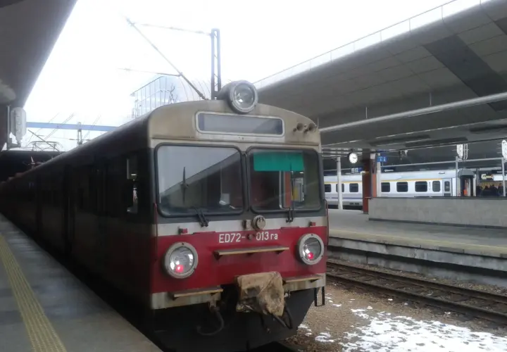 Pociąg ED72-013 ra stoi na peronie. W tle widać nowoczesny budynek dworca i inne pociągi.