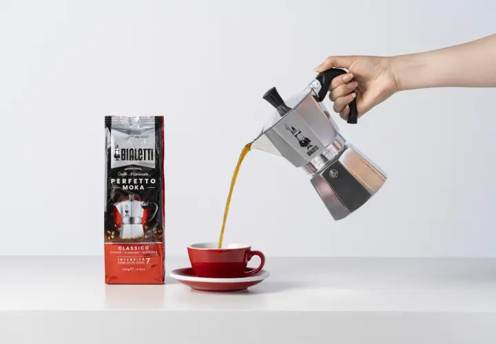 Aromatyczne espresso z kawiarki Bialetti trafia do czerwonej filiżanki. Obok stoi paczka kawy Perfetto Moka.