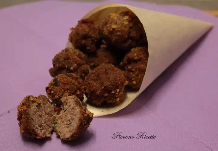 Un cono di carta pieno di polpette fritte dorate, una tagliata a metà rivela un interno succoso.