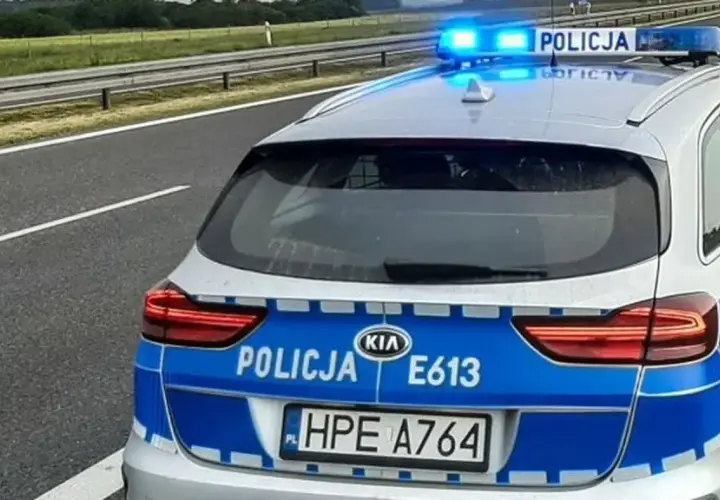 Policyjny pojazd uprzywilejowany z włączonymi niebieskimi światłami stoi na poboczu autostrady.