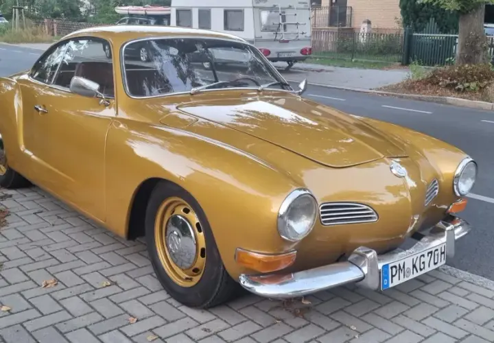 Złoty Karmann Ghia, klasyk z lat 60., lśni na tle ulicy.