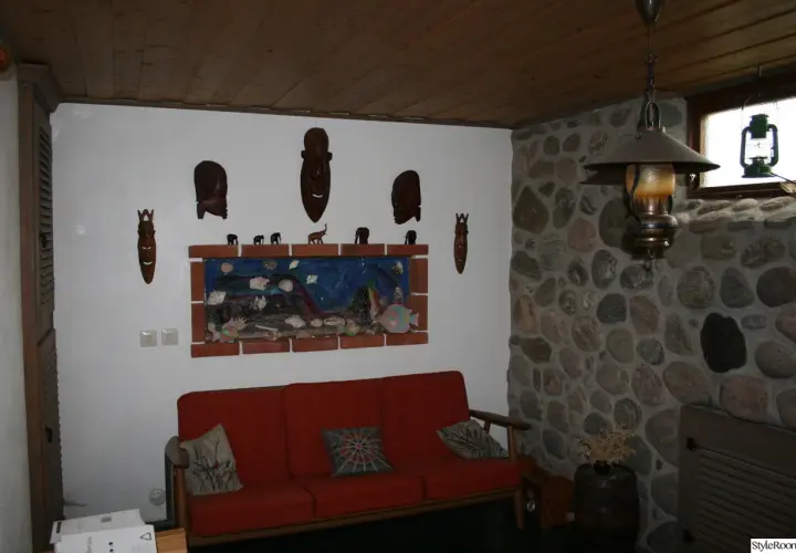 Gillestuga inspiration med en röd soffa, konstverk med afrikanska masker och stenklädd vägg.