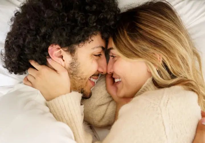 Coppia in un abbraccio intimo, sorrisi e sguardi complici. Un momento di tenerezza e sesso a coppia che celebra l'amore.