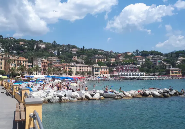 Plage animée à Santa Margherita Ligure, Italie, avec des parasols colorés, des baigneurs sur les rochers et des bâtiments pittoresques à flanc de colline.