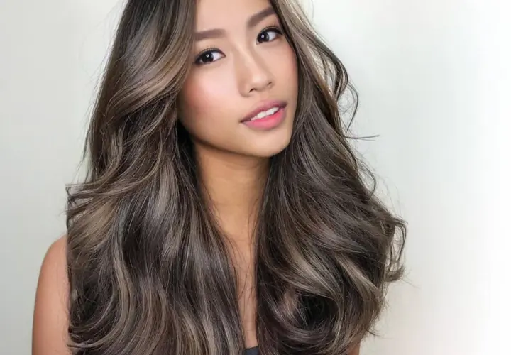 Mujer con cabello castaño con reflejos claros, ondulado y brillante. Descubre cómo dar brillo al pelo teñido para un look radiante.