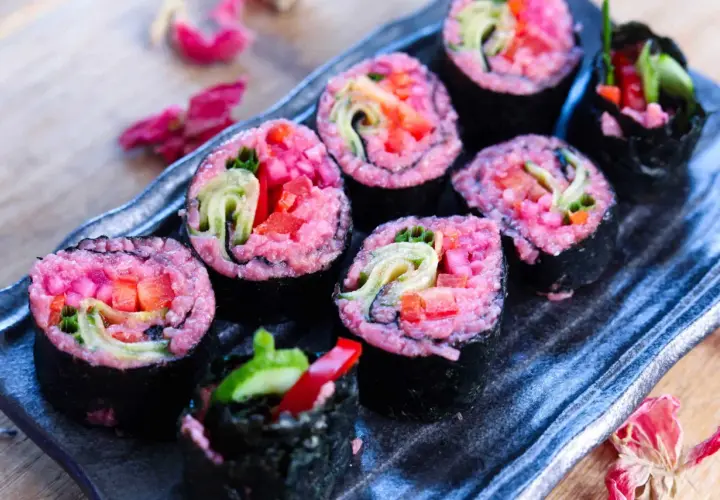Sushi rolls with vibrant pink rice, filled with fresh vegetables like cucumber and red pepper. A delightful pink rice recipe for a colorful meal.