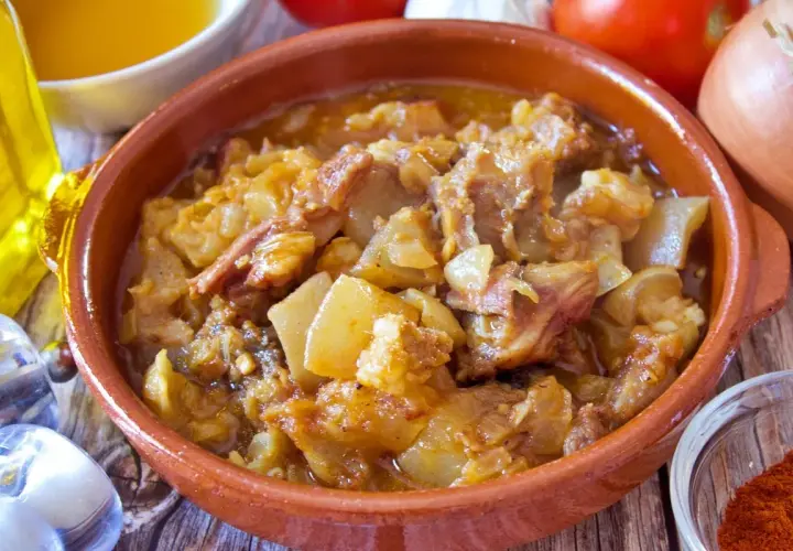 Guiso de cap i pota en cazuela de barro, con patatas y trozos de carne, acompañado de ingredientes frescos.