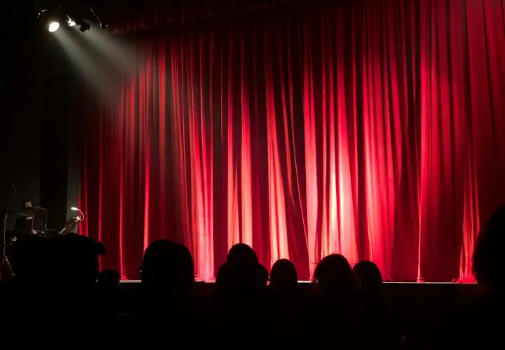 Czerwona kurtyna w teatrze współczesnym w Warszawie. Widownia w mroku, światło reflektora na scenie.