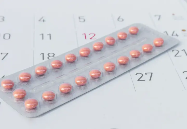 Blister z różowymi tabletkami antykoncepcyjnymi leży na kalendarzu, symbolizując różne rodzaje tabletek antykoncepcyjnych i planowanie.