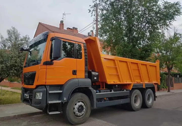 Pomarańczowa wywrotka, idealna do transportu materiałów budowlanych. Z kategorią C można ciągnąć taką przyczepę.